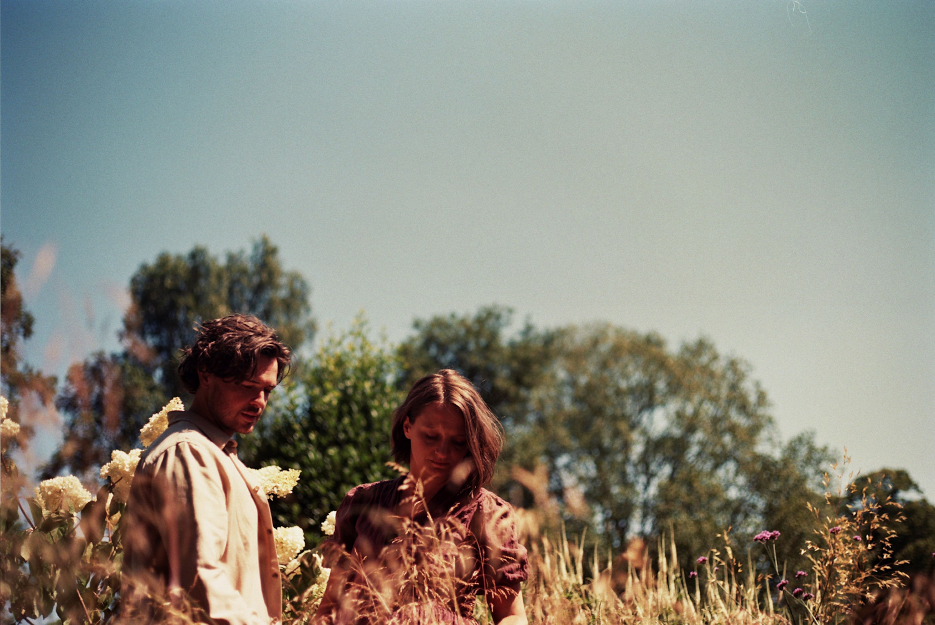 Sam and Beth of The Goudies standing in long summer grass under a pale sky